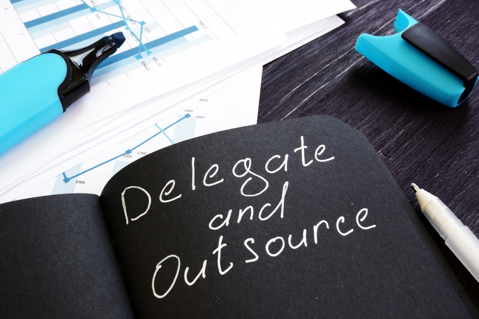 Delegate and Outsource written on a black page. Delegation cincept.
